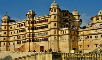 The City Palace in Udaipur, a large,  building with domes, under a bright sky. 