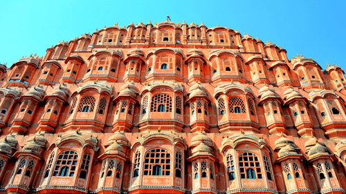 The intricate windows of the Hawa Mahal in Jaipur getting highlighted by the bright sun rays against a clear blue sky in the background.