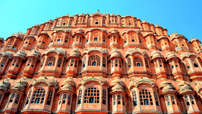 The intricate windows of the Hawa Mahal in Jaipur getting highlighted by the bright sun rays against a clear blue sky in the background.