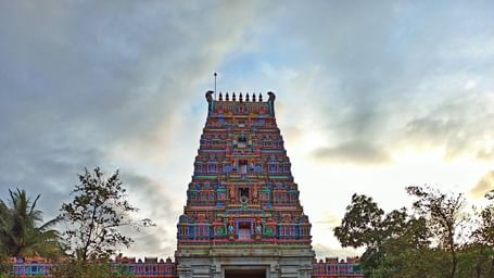 A large, multi-level red temple tower with a long, paved walkway leading to it under a partly cloudy sky.