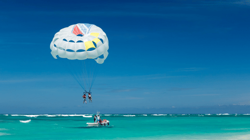 Two people parasailing above turquoise waters while being towed by a speedboat during a water sports adventure in Goa.