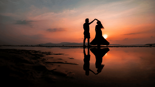 Two people dancing at a beach with a sunset in the background.