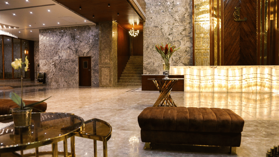 The lobby area of Leroy Grand, Yeshwanthour, overlooking the reception desk illuminated with bright lights along with cushioned seating area in the foreground.