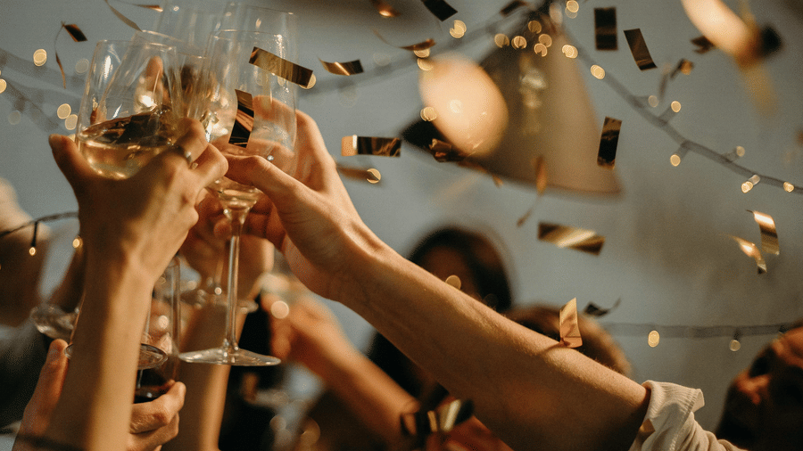 Guests raise champagne glasses amid confetti, celebrating New Year with a joyful toast at an elegant party.