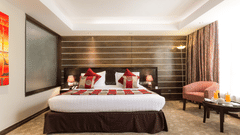 Deluxe Room with king size bed, red cushions, wooden accent wall, armchair with table, carpet flooring, and warm lighting at Boma Inn Eldoret