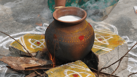 An overview of a clay pot with milk in it being boiled outdoors for Pongal 2026.