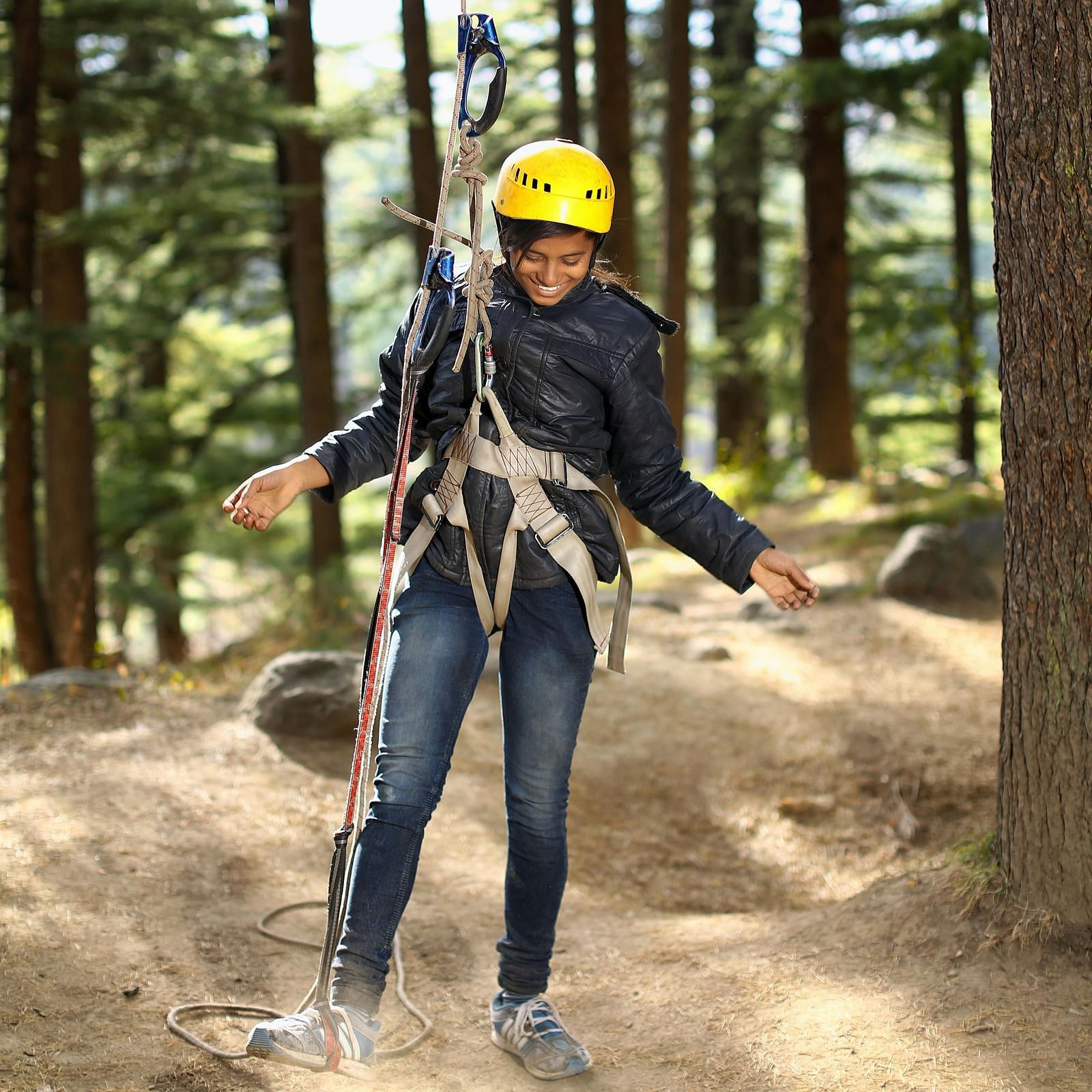 A close-up view of a woman hanging from a zipline rope, set against a backdrop of lush greenery in the forest.