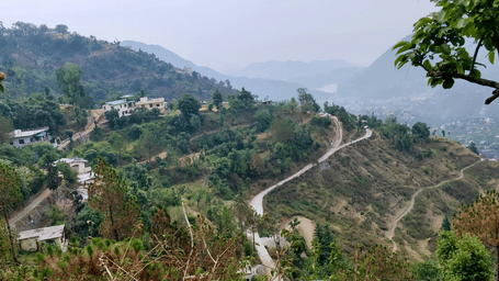 Winding mountain road on a trip from Dehradun to Auli passing through green hills and scattered homes under a clear sky