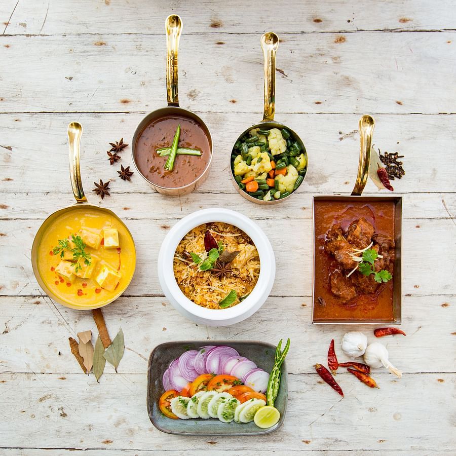 Food presentation of biryani, paneer curry, vegetables and meat curry, and sliced onions