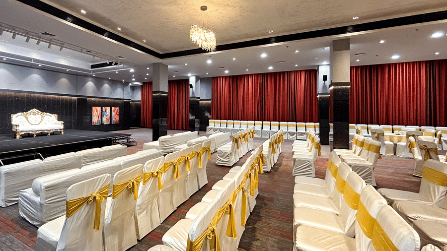 Banquet hall with red curtains, carpet floor, and golden & white cloth draped chairs in rows at Infiniti Hotel, Indore.