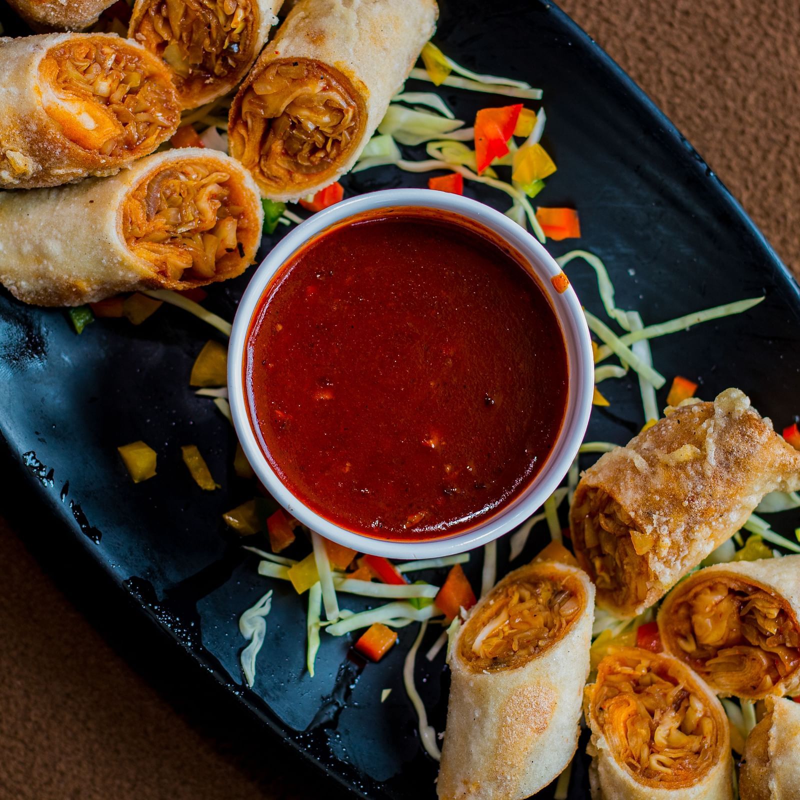 A serving of spring rolls arranged around a small bowl of dipping sauce.