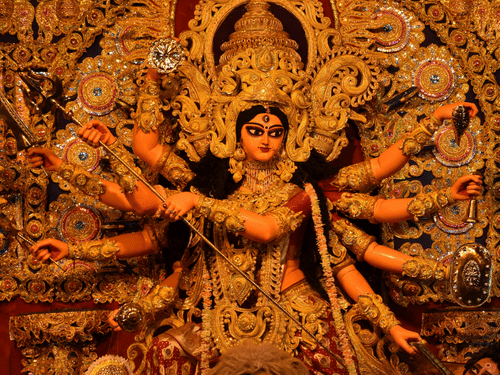 An intricate statue of Goddess Durga, adorned in gold ornaments, depicted in a powerful pose.