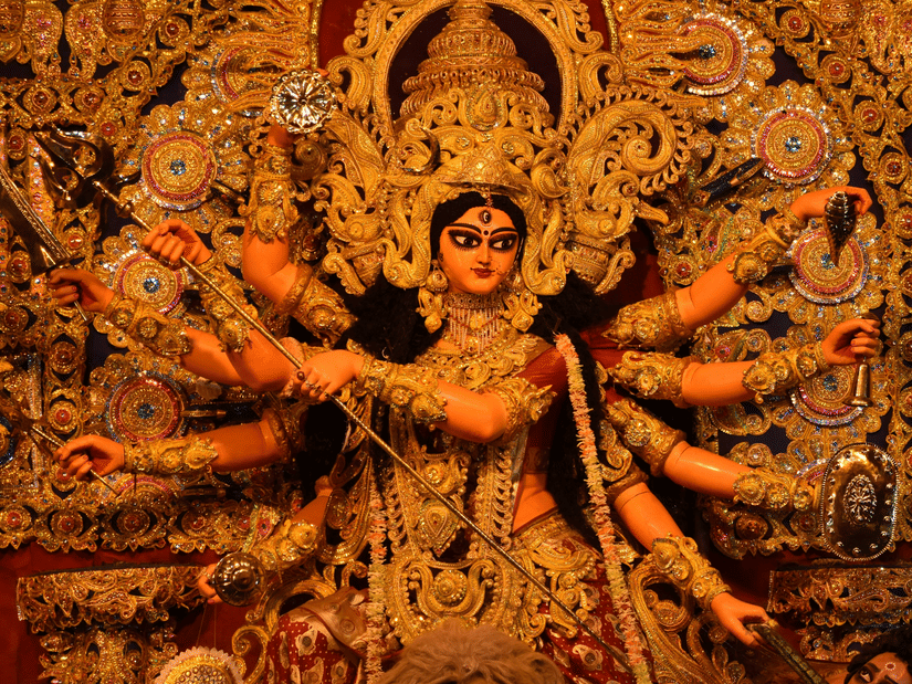 An intricate statue of Goddess Durga, adorned in gold ornaments, depicted in a powerful pose.