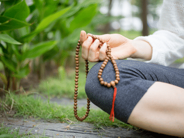 Close-up of a hand holding prayer beads during a meditation practice outdoors.