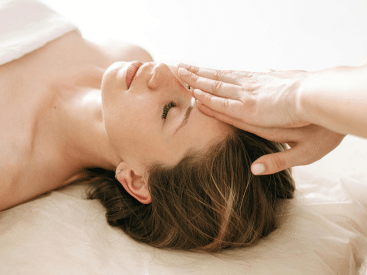 Close-up of a woman's face with a hand gently resting on her forehead.