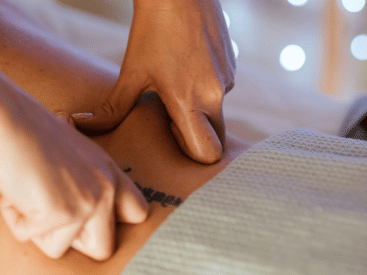 A masseur's hands applying pressure to someone's calf muscle.