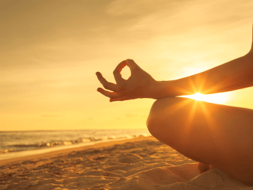 A close-up of a meditation gesture at sunset on the beach.
