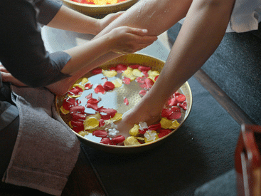 A person soaking their feet in a bowl filled with water and rose petals.