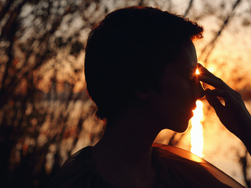 Silhouette of a person touching their forehead against a sunset backdrop.