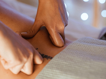 A masseur's hands applying pressure to someone's calf muscle.