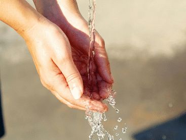 Hands cupping a stream of water outdoors.