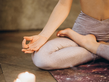 Close-up of a person in a seated lotus yoga pose, wearing light-colored leggings, with one hand resting on the knee in a mudra position.