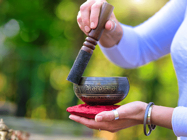 A person using a Tibetan singing bowl outdoors.