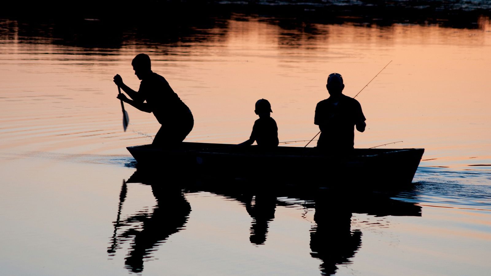 Silhouette of three people in a small boat on calm waters at sunset.