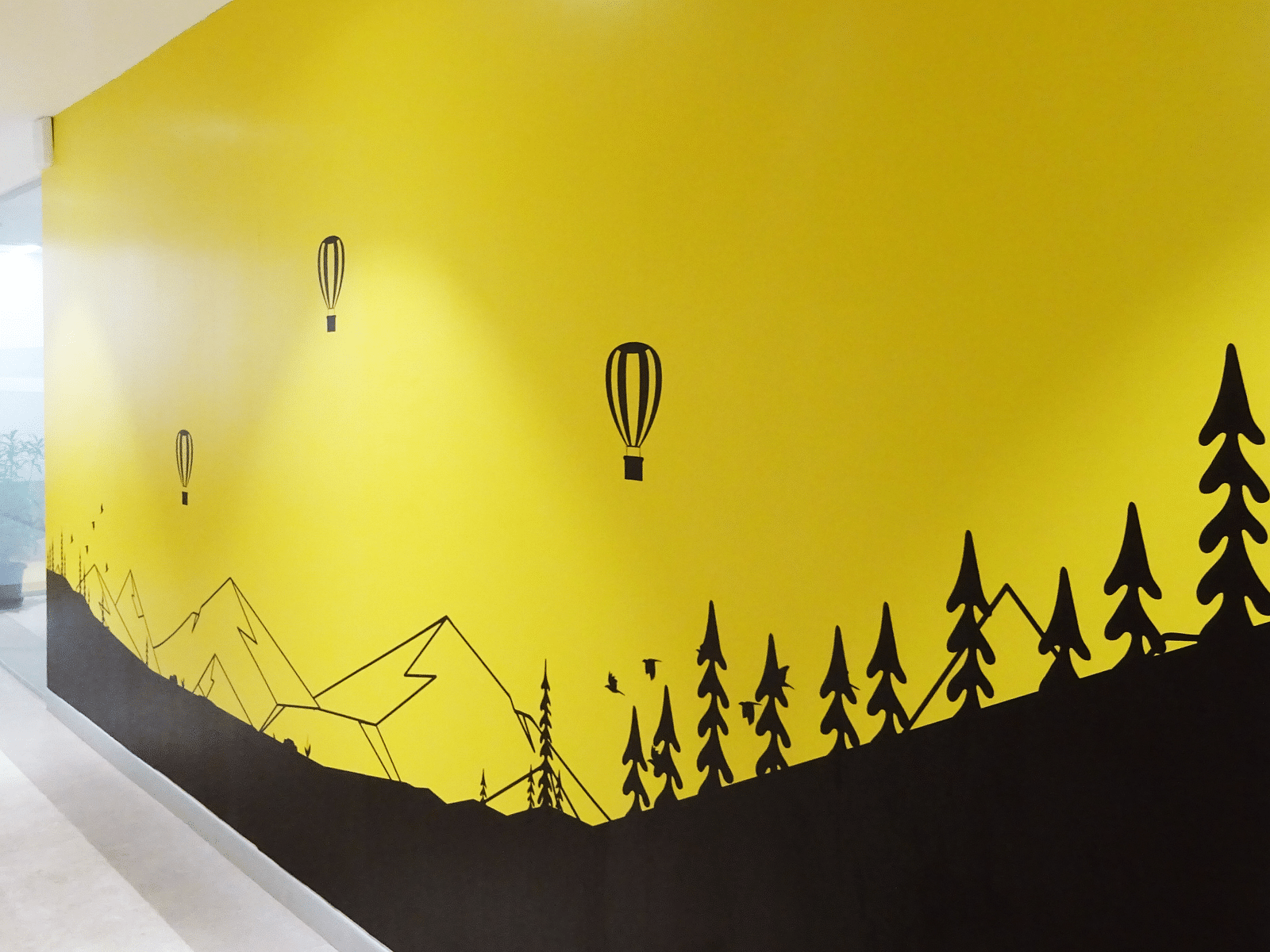 A painted wall with yellow background and three hot air ballons and mountains.