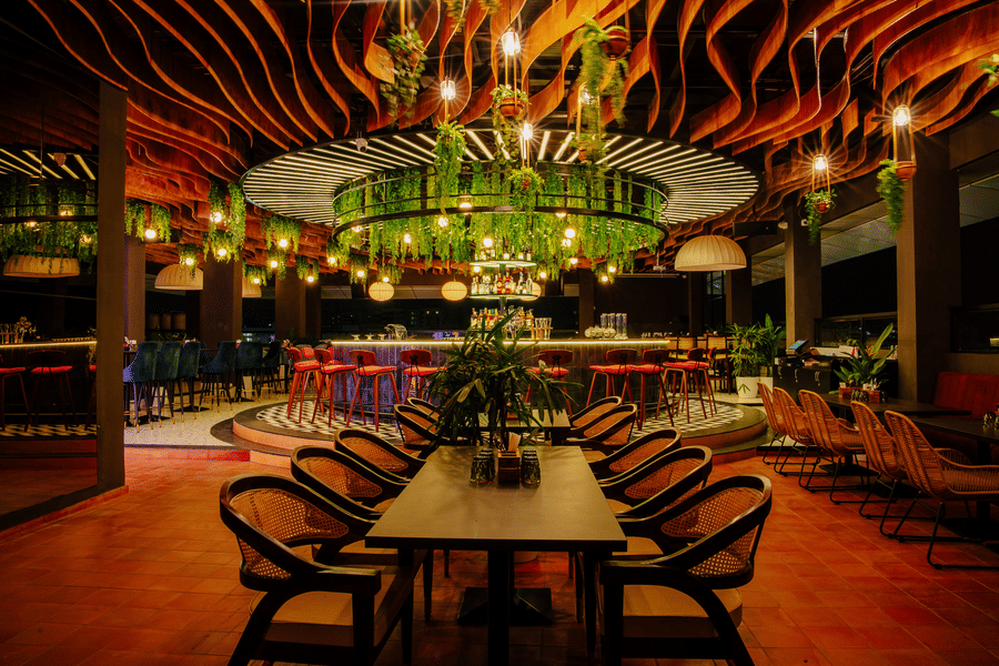 Elegant dining space with a central bar adorned with greenery and warm lighting. |  The Icon Select by Bhagini, Mahadevapura