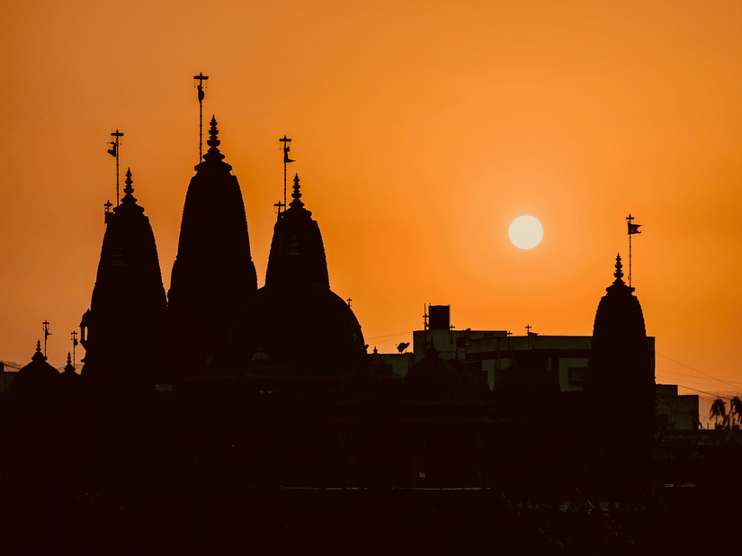 Temple spires form a striking silhouette against a glowing orange sunset sky.