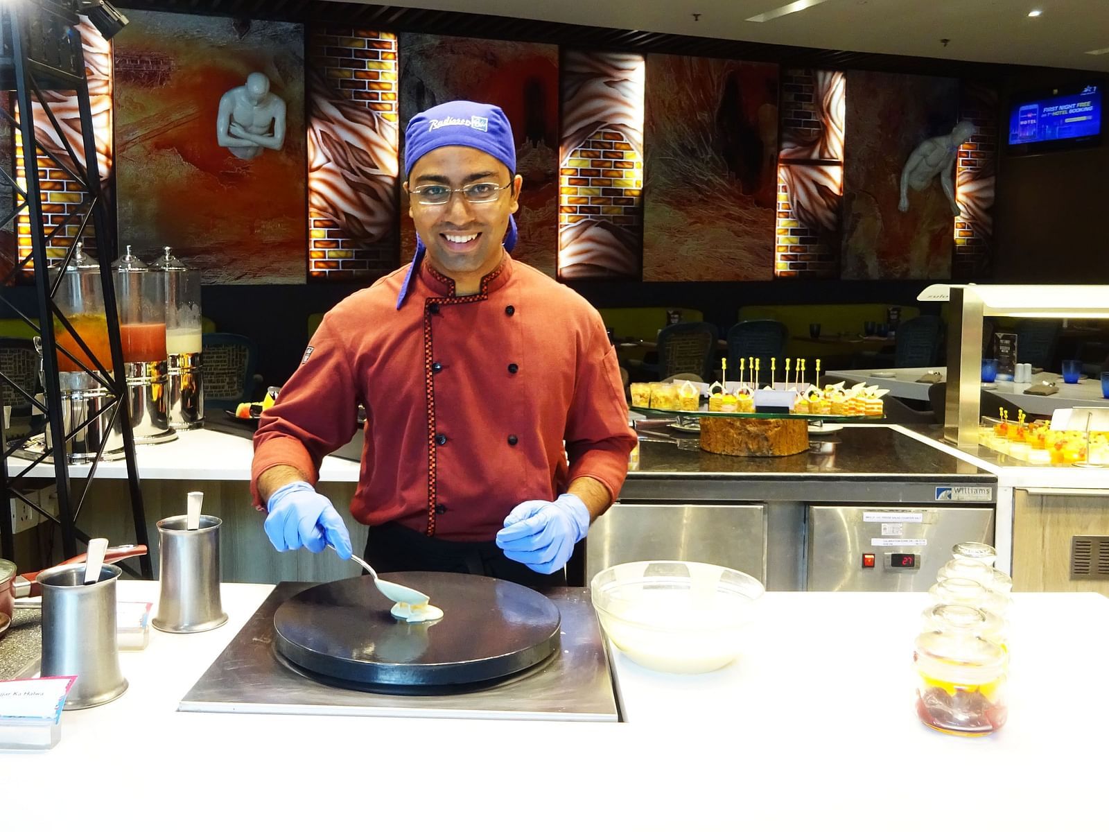 Chef preparing a dish at a live cooking station wearing gloves and a hat.