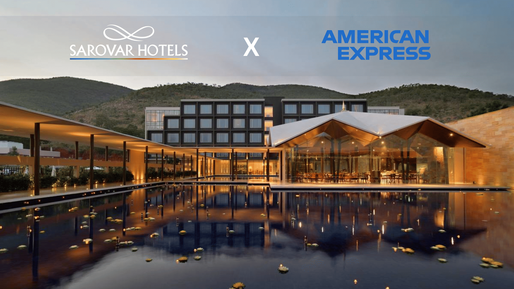 A building with several windows, restaurant with glass walls, and a corridor with plants and lights. A promotion for Amex Card holders at Sarovar Hotels.