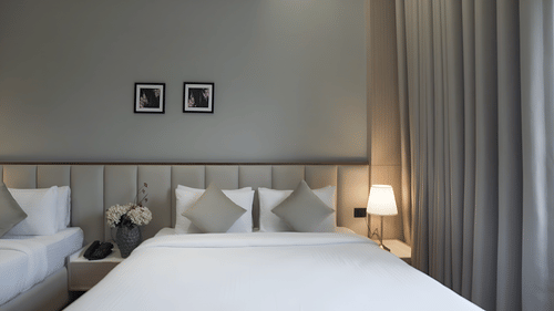 Premium Deluxe bedroom with a double and a single bed with bed side lamps lit besides them during the daytime at Pride Resort, Rajkot