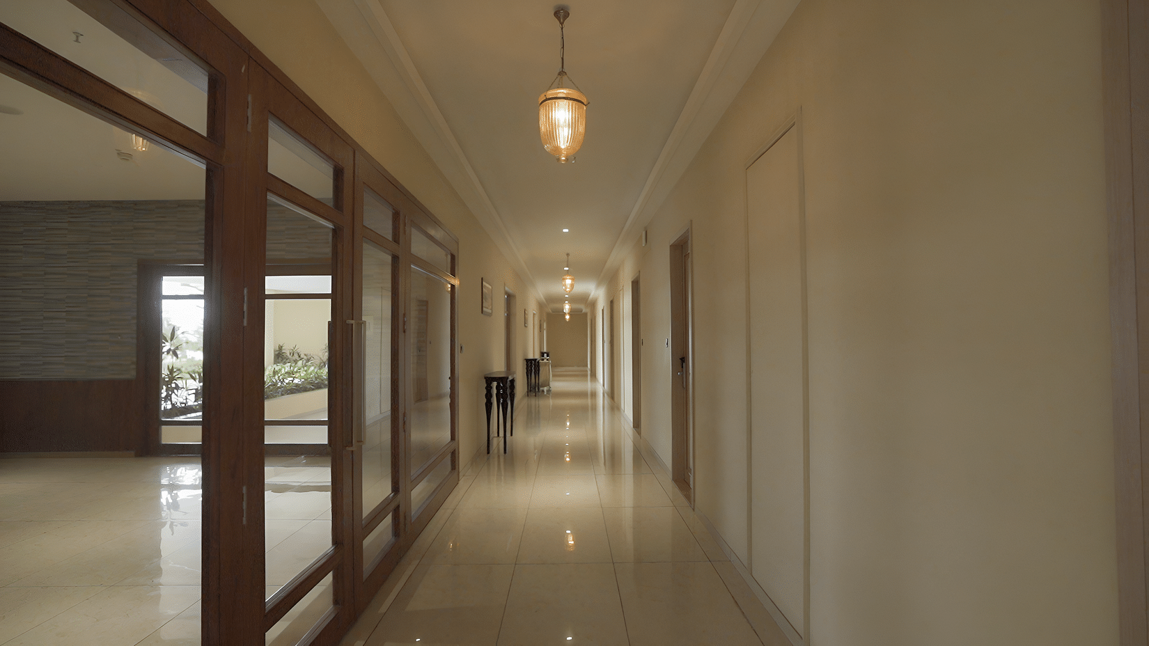 A well-lit hotel hallway at Pride Resort, Rajkot featuring light-coloured walls and a reflective surface on the right