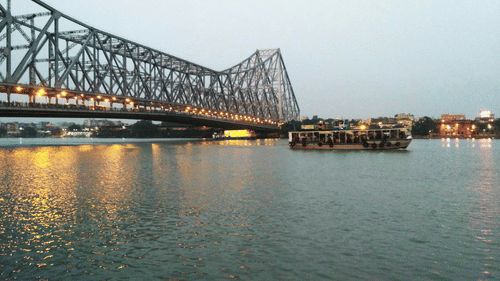An overview of howrah bridge on the banks of hooghly river with a boat on the river
