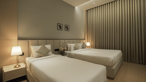 Premium Deluxe bedroom with a double and a single bed with bed side lamps lit besides them - Pride Resort, Rajkot