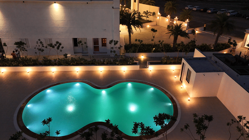 Aerial shot of the swimming pool in an infinity shape with night lights illuminating the area - Pride Resort, Rajkot