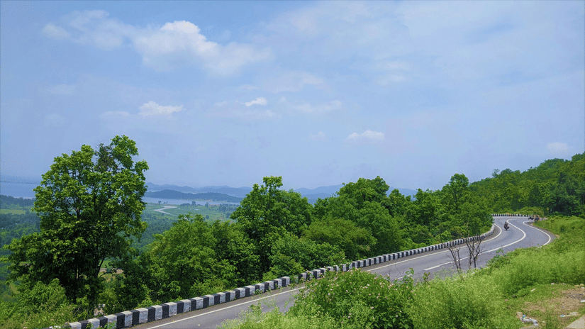 A winding road with greenery around and white clouds on blue sky in the background