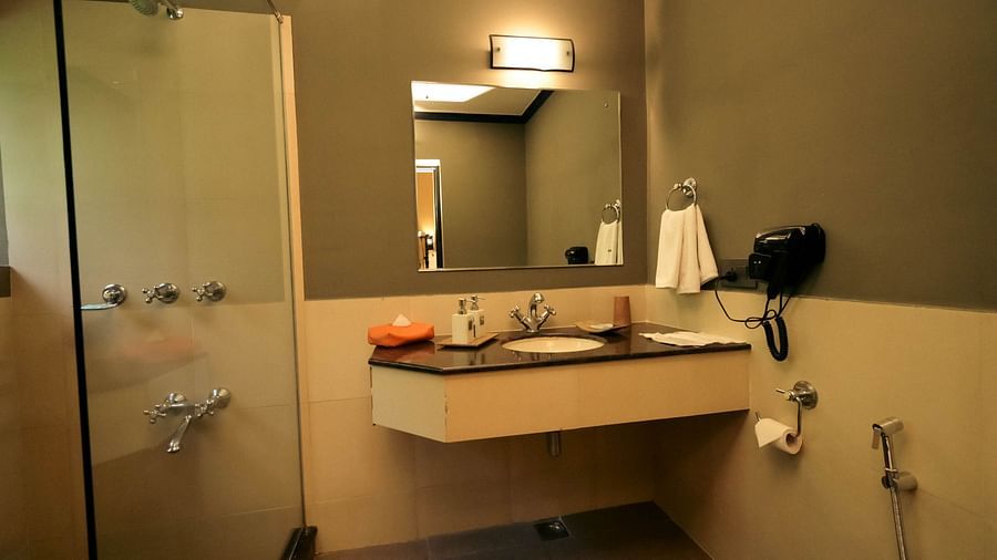 Bathroom of Superior Cottage at Clarks Safari, Pushkar featuring a large mirror over the sink with toiletries on the slab and a hair dryer next to it on the wall