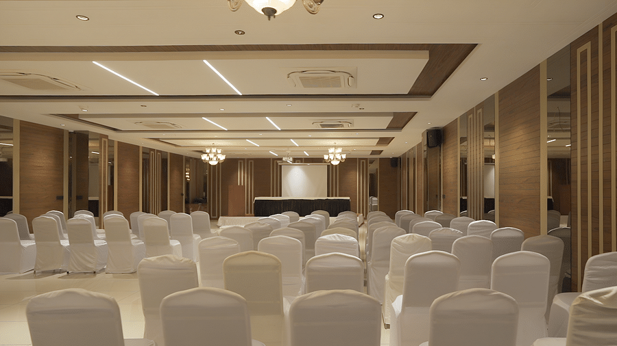 An expansive banquet hall with white coloured chais arranged facing towards the stage - Pride Resort, Rajkot