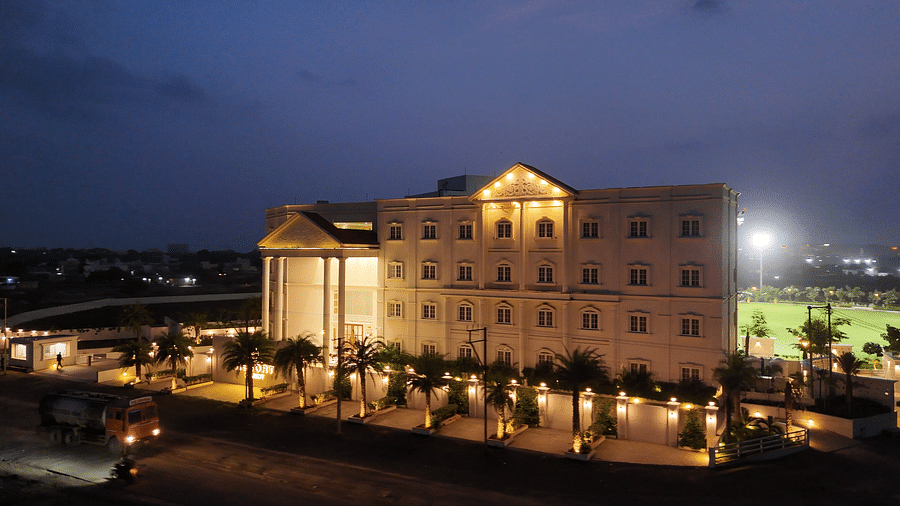 An aerial night view of a brightly lit Pride Resort, Rajkot featuring a swimming pool and a lawn, illuminating the dark surroundings