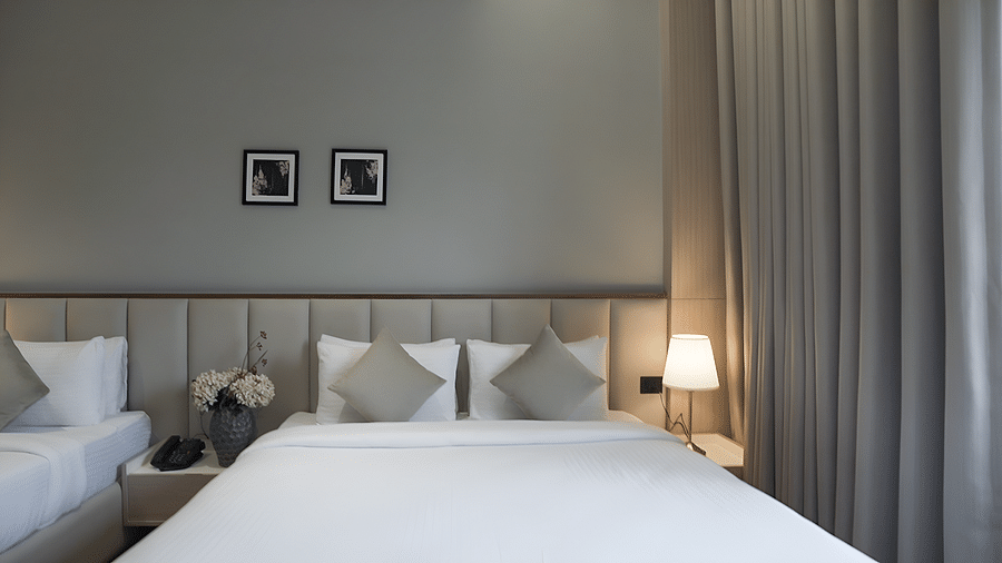 Close up view of Premium Deluxe bedroom with a double and a single bed with bed side lamps lit besides them taken during the day - Pride Resort, Rajkot
