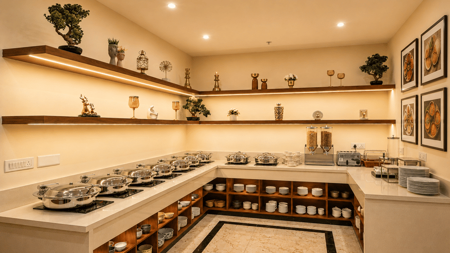 Buffet counter at Tulip Inn, Hoodi Whitefield, Bengaluru, showing serving dishes, shelves with crockery, glass items, and wall frames.