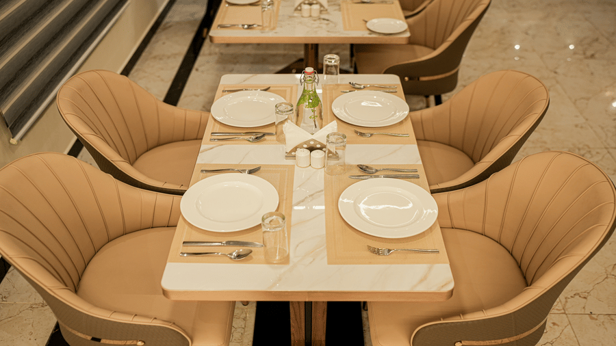 Dining table at Tulip Inn, Hoodi Whitefield, Bengaluru, set with plates, cutlery, glasses, and 4 cushioned armchairs.
