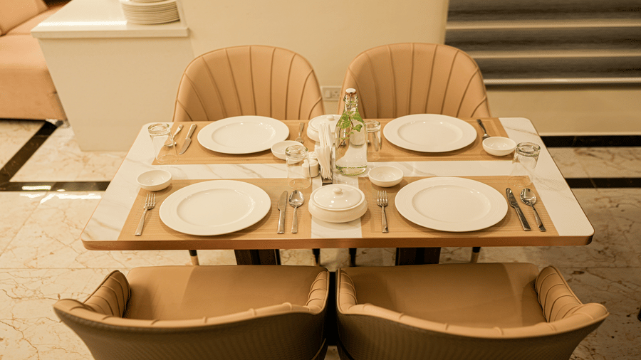 Table setting at Tulip Inn, Hoodi Whitefield, Bengaluru, featuring plates, cutlery, placemats, glasses, and surrounding armchairs.