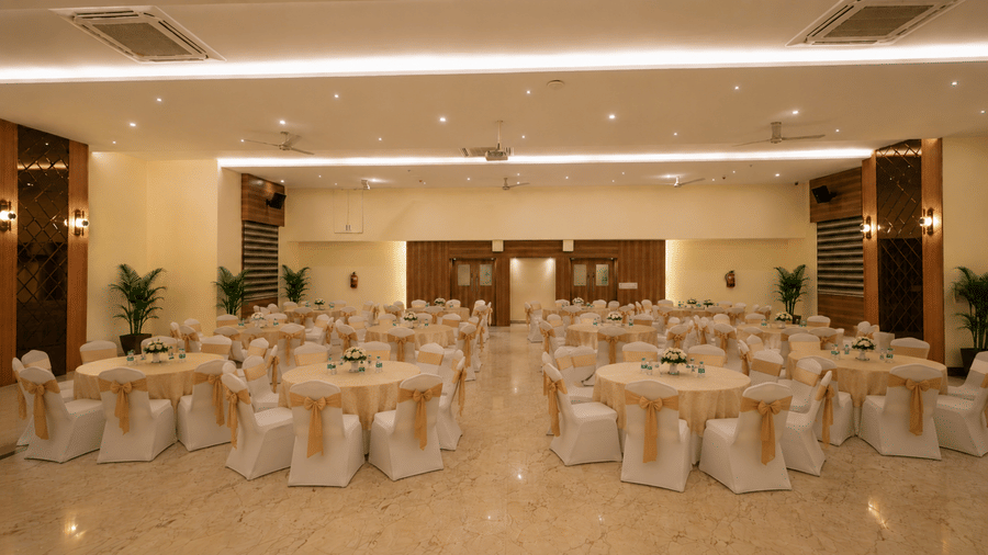 Lavender banquet hall at Tulip Inn, Hoodi Whitefield, Bengaluru, set up with round tables, chairs, covers, ties, and indoor potted plants.