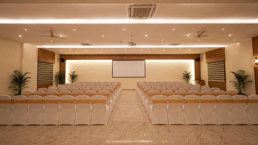 Theater style event space at Tulip Inn, Hoodi Whitefield, Bengaluru, set up with rows of chairs facing a projector screen at the head of the room.