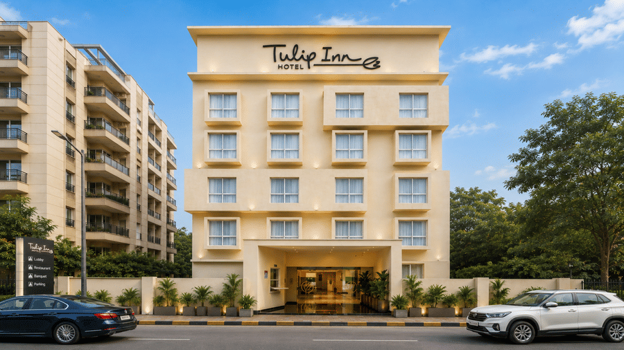 Daytime exterior shot of Tulip Inn, Hoodi Whitefield, Bengaluru, showing the building facade, a driveway, vehicles, and foliage.