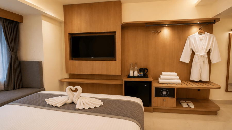 Standard Room at Tulip Inn, Hoodi Whitefield, Bengaluru, showing a bed with towel swans, a television, a mini fridge, and a bathrobe on a hanger.